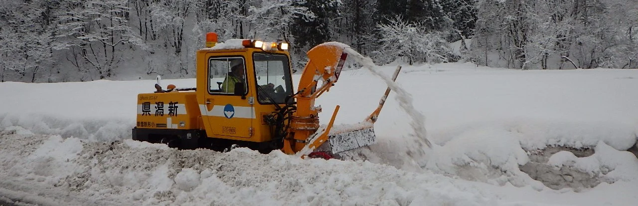 雪の積もった歩道で稼働する黄色い除雪機